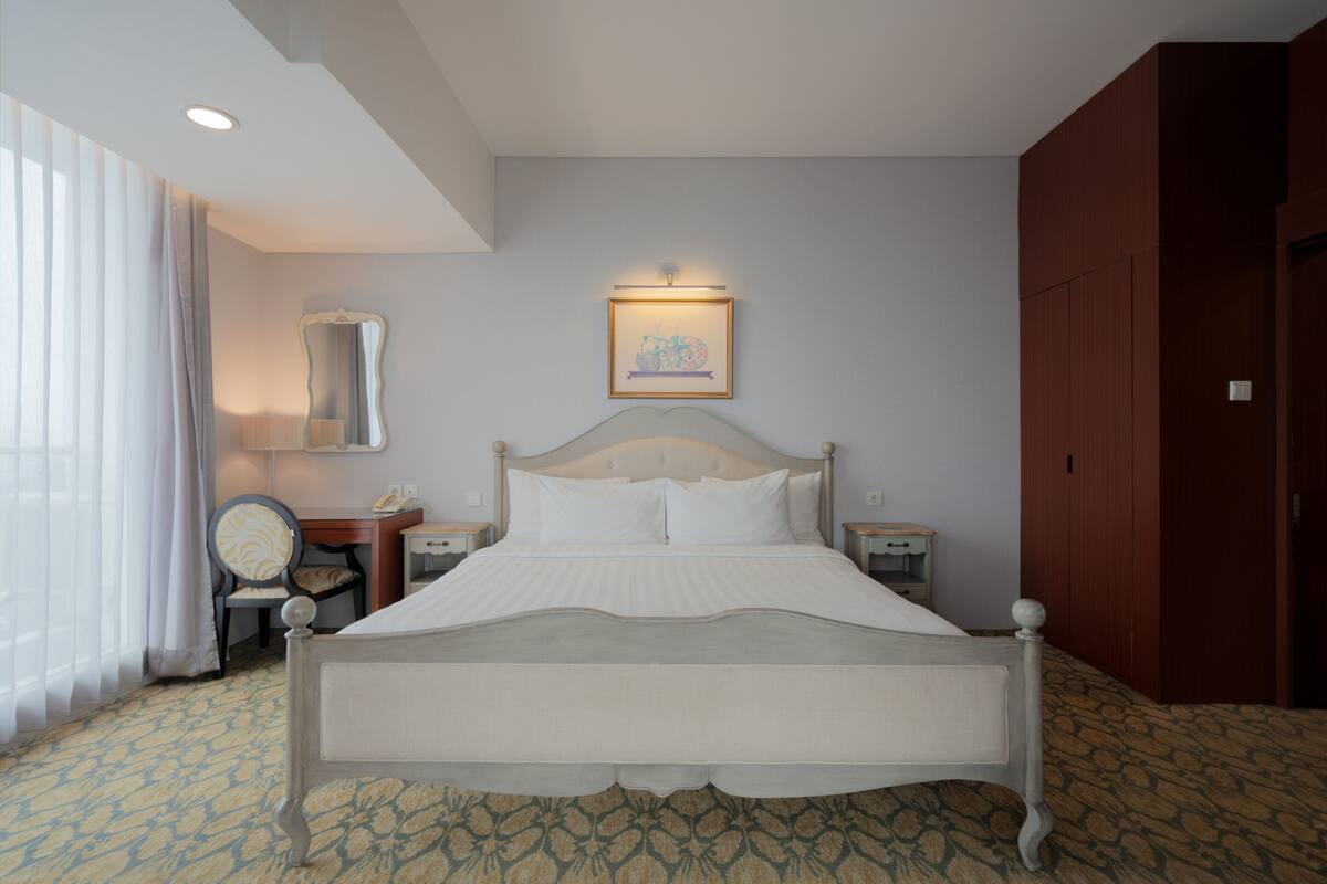Una habitación de hotel con una cama grande, una mesita de noche, una silla, un espejo y un armario.