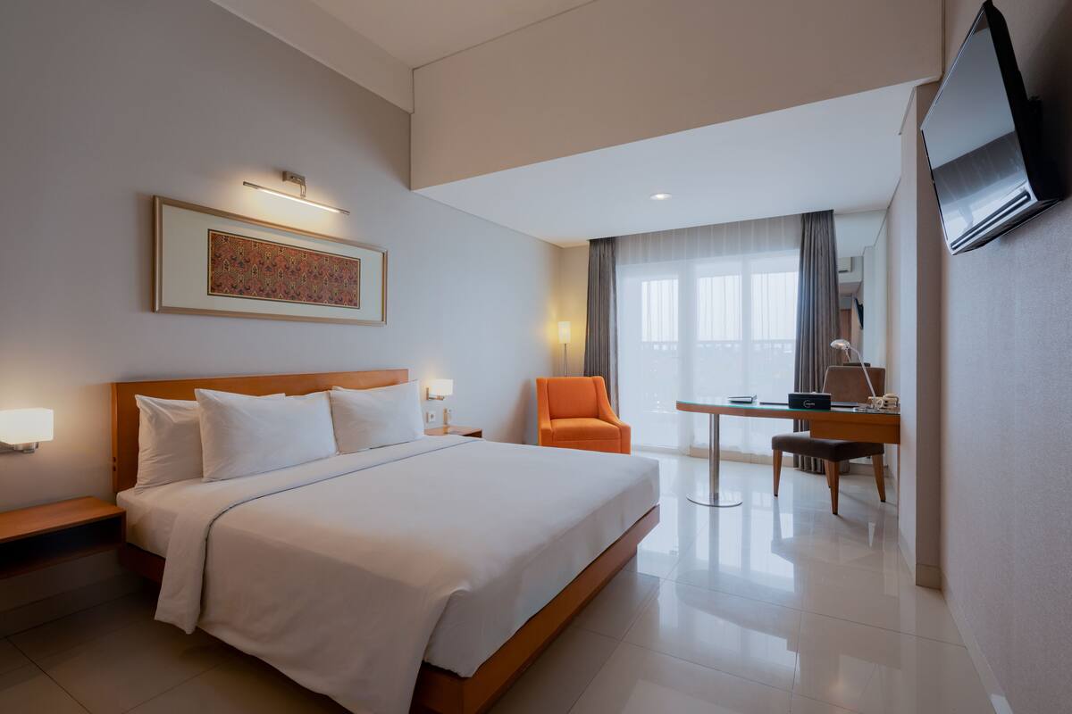 Habitación de hotel con una cama grande, un escritorio, una silla, un televisor y un cuadro en la pared.