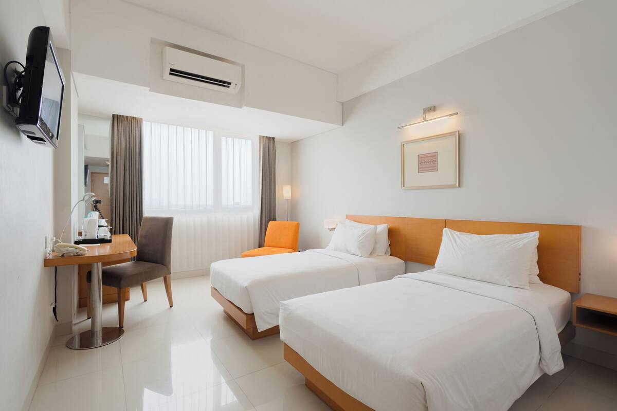 Una habitación de hotel con dos camas, un escritorio con silla, un televisor y un cuadro en la pared.