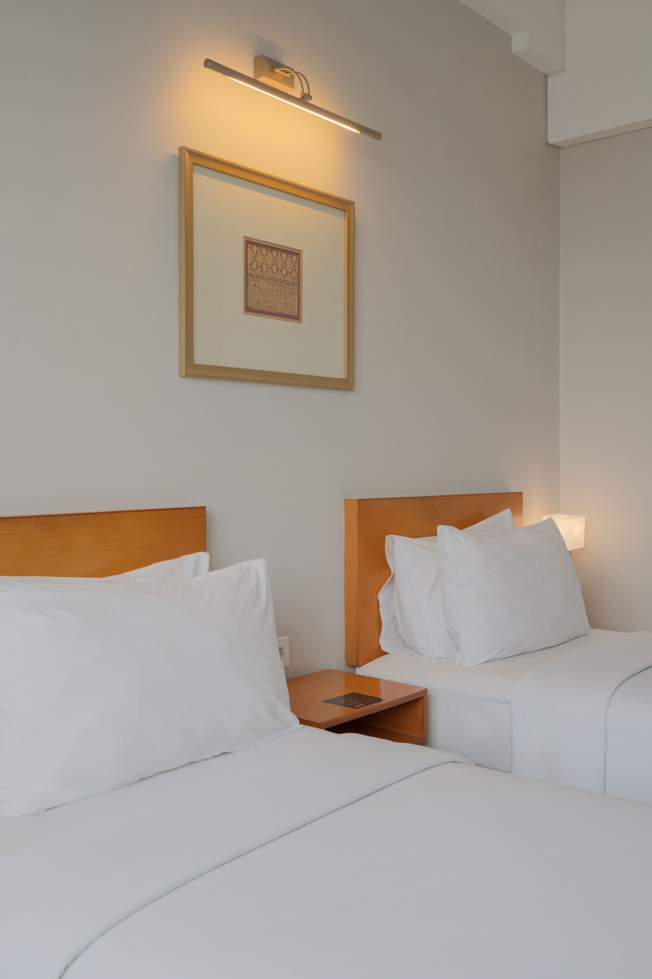 A hotel room with two beds, a nightstand, a framed picture on the wall, and a wall-mounted light fixture.