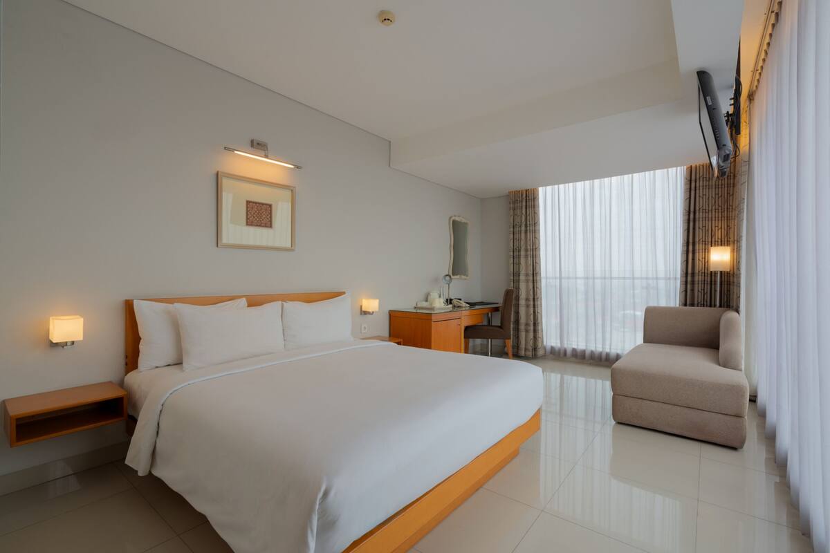 Una habitación de hotel con una cama grande, un escritorio, una silla y una ventana con cortinas.