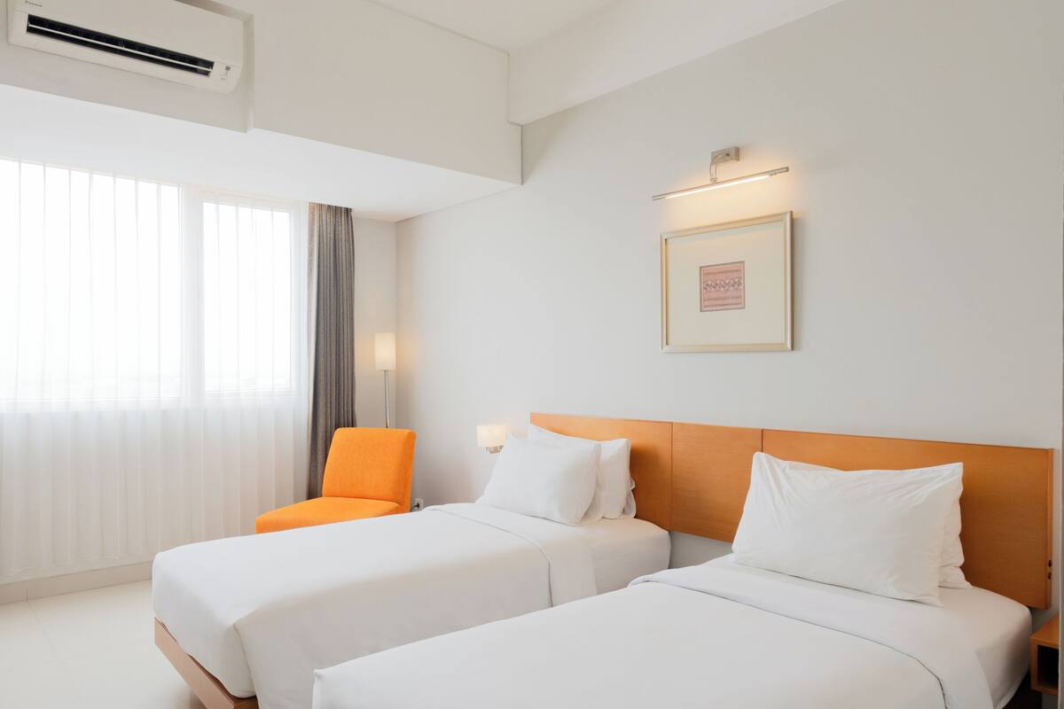 Habitación de hotel con dos camas, una silla, un equipo de aire acondicionado y un cuadro en la pared.