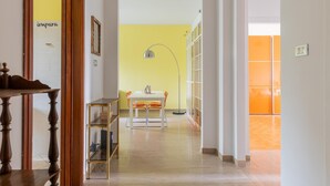 A hallway with a wooden table, a white table with orange chairs, a floor lamp, and a bookshelf. - Casa Limone by Wonderful Italy (Bologna)