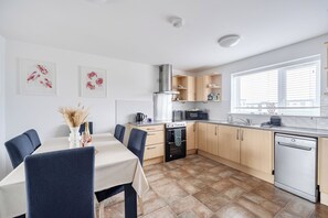 A modern kitchen with a dining area, featuring a stove, microwave, and dishwasher. - Spacious 3 Bed House - Sleeps 6 - Parking - Wifi (Newquay)