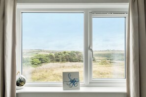 A window with a view of a landscape, a curtain, and a small framed artwork. - Spacious 3 Bed House - Sleeps 6 - Parking - Wifi (Newquay)