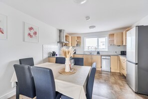 A modern kitchen with a dining table, chairs, and a dishwasher. - Spacious 3 Bed House - Sleeps 6 - Parking - Wifi (Newquay)