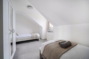 A bedroom with a sloped ceiling, a bed with a brown blanket, a bedside table with a picture, and a wardrobe. - Spacious 3 Bed House - Sleeps 6 - Parking - Wifi (Newquay)