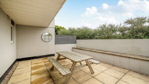 A patio with a wooden table and benches, a round mirror, and a view of greenery. - Spacious 3 Bed House - Sleeps 6 - Parking - Wifi (Newquay)