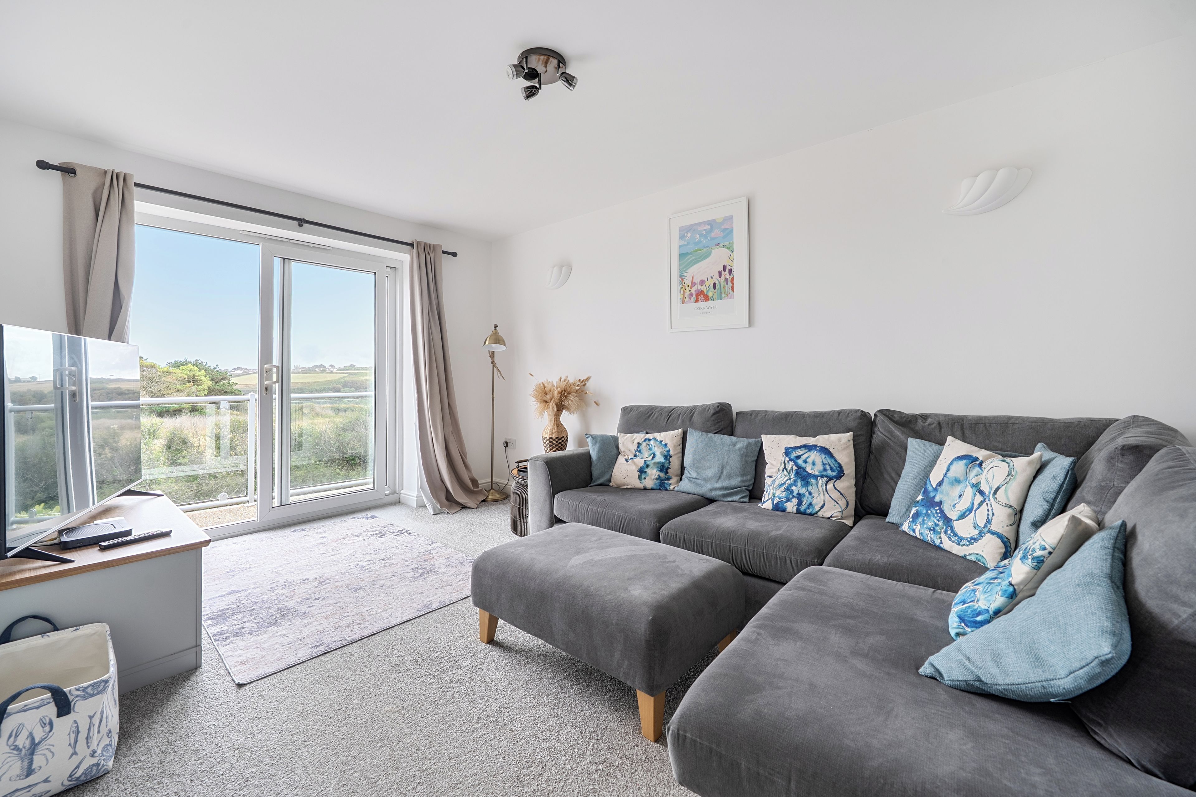 A modern living room with a grey sofa, a flat-screen TV, and a large window with curtains.