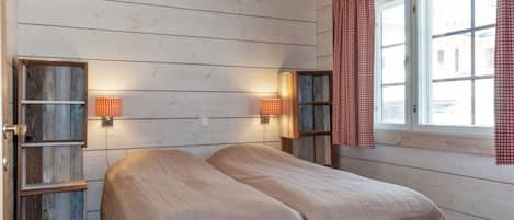 A room with a bed, two wall-mounted lamps, and a window with curtains.