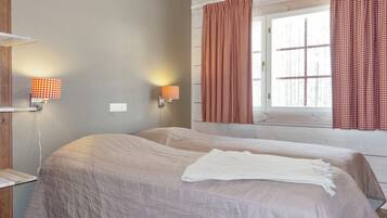 A room with two beds, a window with curtains, and wall-mounted lamps.
