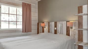A bedroom with a large bed, wooden panel walls, and a window with a view of trees.