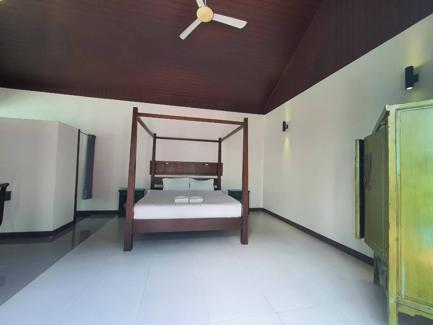 A bedroom with a four-poster bed, a ceiling fan, a wardrobe, and a door.