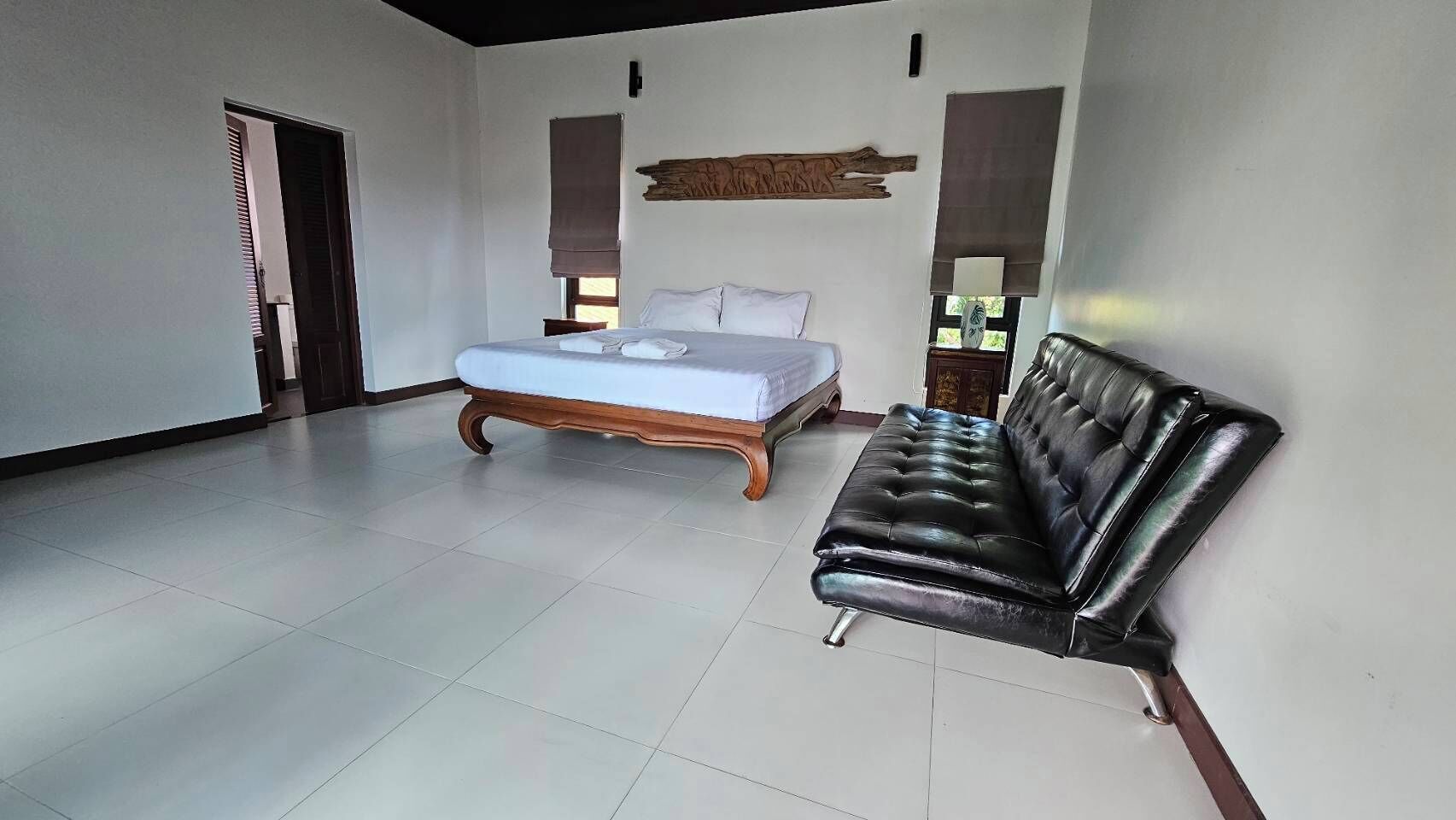A spacious room with a bed, a black leather sofa, and a wooden headboard.