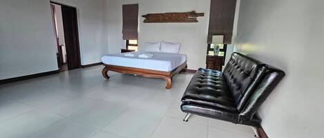 A spacious room with a bed, a black leather sofa, and a wooden headboard.