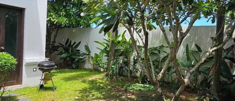 Un patio trasero residencial con piscina, una parrilla para barbacoa y diversas plantas.