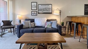 Una sala de estar con un sofá azul oscuro, una mesa de centro de madera y una lámpara de pared.