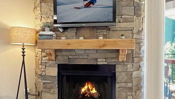 Una chimenea de piedra con un televisor de pantalla plana encima, un estante de madera y suelo de baldosas.