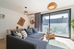 A modern living room with a grey sofa, a round coffee table, and a large window offering a view of the city.
