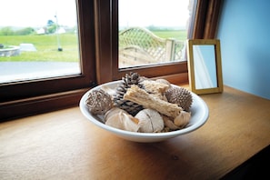 Eine Schüssel mit natürlichen Gegenständen auf einem Holztisch neben einem Fenster mit Blick auf eine grüne Landschaft.