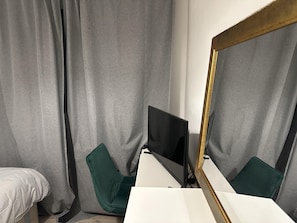A room with a bed, a desk with a computer, a chair, and a large mirror.