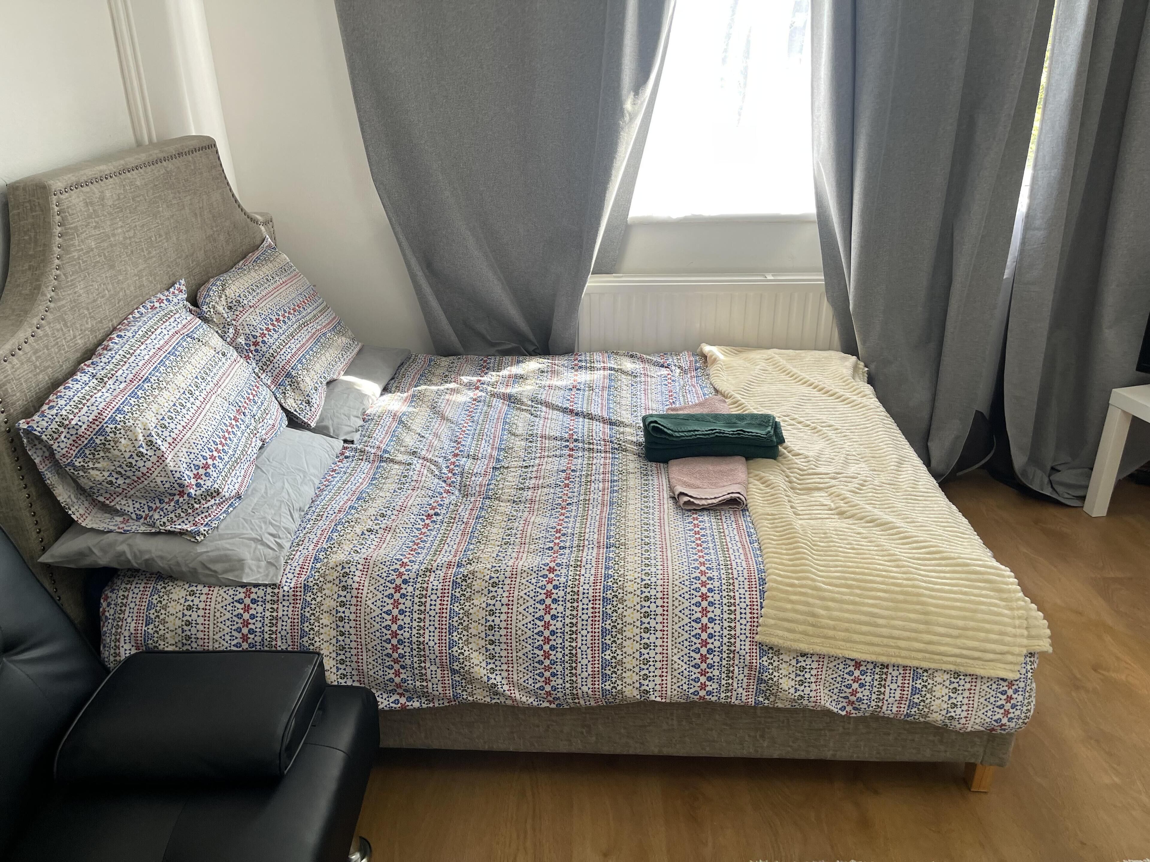 A bed with a patterned bedspread, pillows, and a folded blanket.