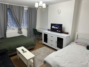 A bedroom with two beds, a desk, a chair, a TV, and a clock on the wall.
