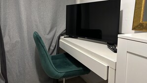 A room with a flat-screen TV on a white desk, a green chair, and a curtain. - Great 5-bed Wembley Home 25min From Central London (Harrow)