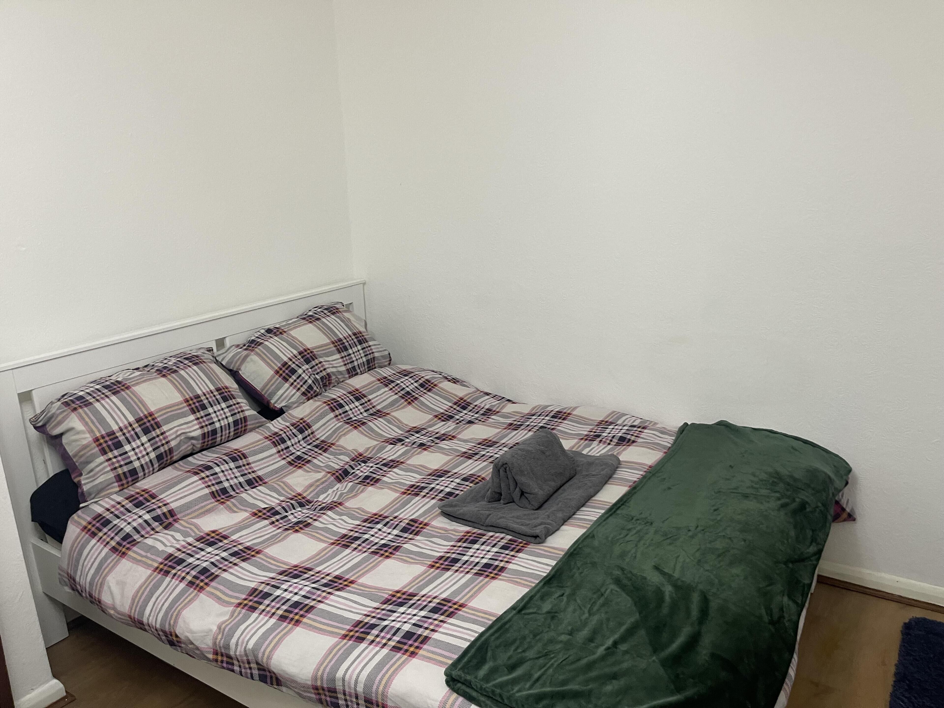 A single bed with a plaid bedspread and a green blanket.