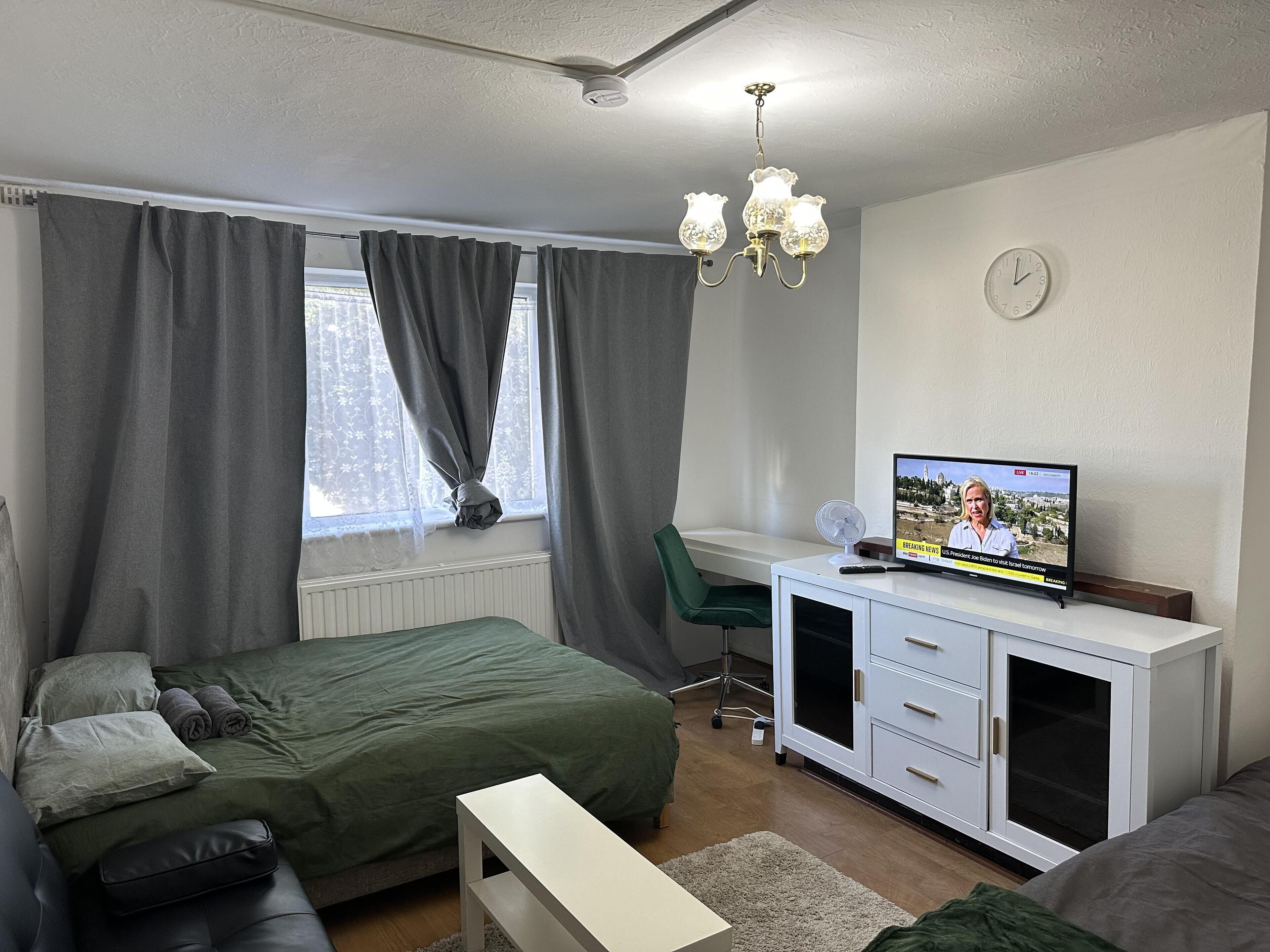Un dormitorio con cama, escritorio, silla, televisor y ventana con cortinas.