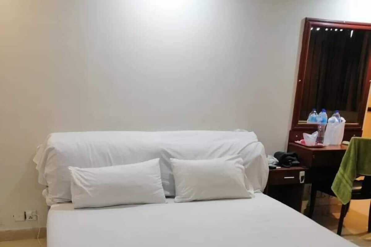 A hotel room with a large bed, a wooden nightstand, a desk, and a mirror.