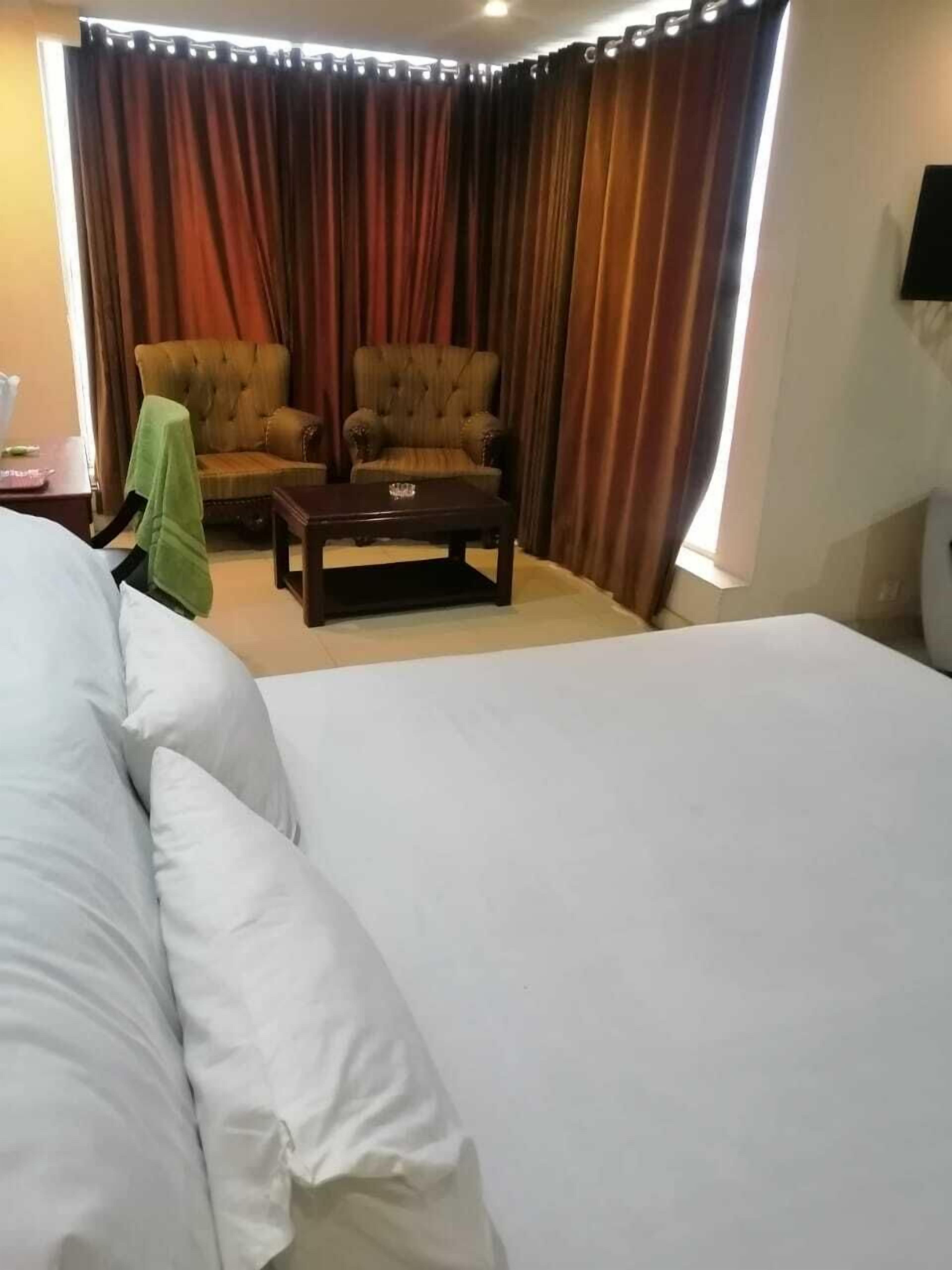A hotel room with a large bed, two armchairs, a small table, and a window with curtains.