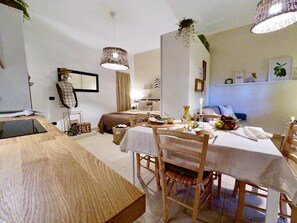A compact, well-lit room with a dining table set for two, a bed with a headboard, and a small kitchenette area. - Studio in basement  equipped with all comforts (Stibbio)