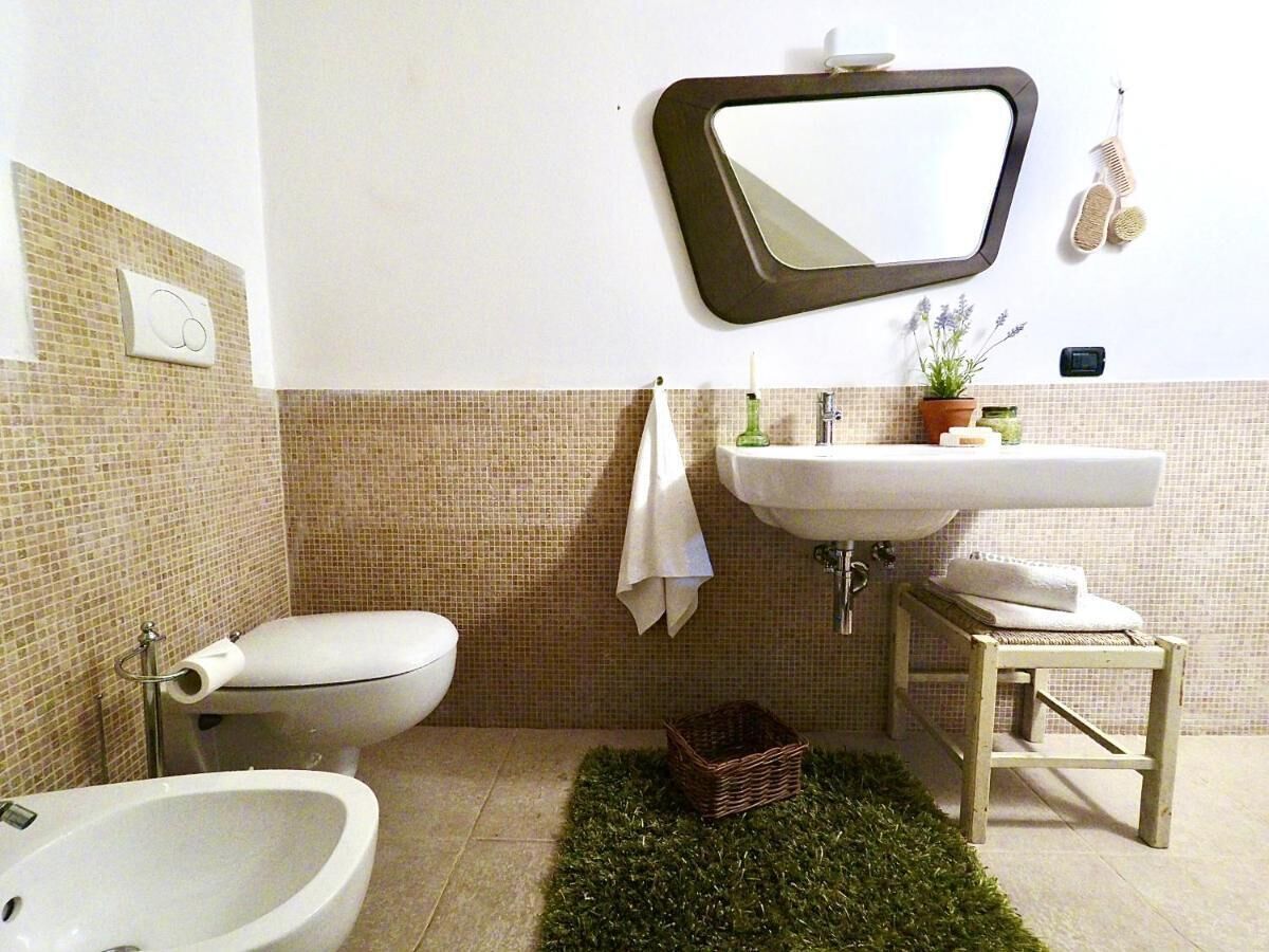 A bathroom with a toilet, bidet, sink, mirror, and a small stool.