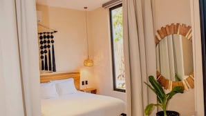 A hotel room with a bed, a sofa, a potted plant, a mirror, and a window with curtains. - Studio Private Pool Natural Lighted Boho Chic (Tulum)