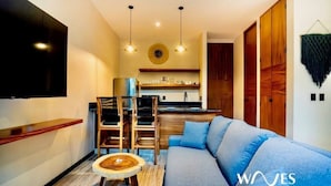 A modern living room with a blue sofa, wooden chairs, a coffee table, and a TV. - Studio Private Pool Natural Lighted Boho Chic (Tulum)