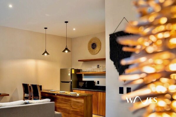 Una cocina moderna con iluminación colgante, una zona de comedor con sofá y un elemento decorativo en la pared.