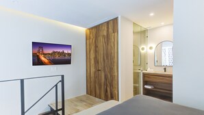 Un dormitorio moderno con cama, armario de madera, baño con espejo y una foto de la ciudad en la pared.