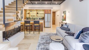 Una sala moderna con una escalera, un sofá, una mesa de centro y una zona de cocina con una mesa de comedor y sillas.