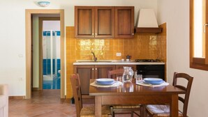 A kitchen with wooden cabinets, a tiled backsplash, a dining table with chairs, and a view of a swimming pool through an open door. - Stunning Residence Bouganvillage Studio Nm1238 (Budoni)