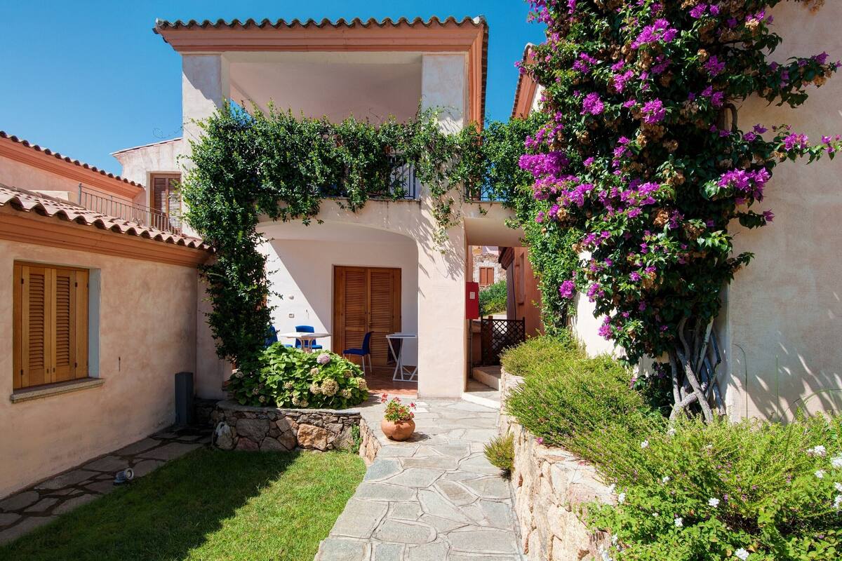 A courtyard with a stone pathway, a wooden door, and a small seating area with a table and chairs.