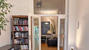 Une pièce moderne avec un bureau en bois, un fauteuil en cuir, une bibliothèque et une vue sur une autre pièce grâce à une porte ouverte.