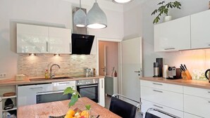 Une cuisine moderne avec des meubles blancs, un four en acier inoxydable et une table à manger en bois sur laquelle est posé un panier de fruits.