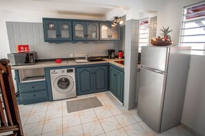 Compact kitchen with a stainless steel refrigerator, washing machine, microwave, coffee maker, and sink.