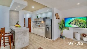 A modern kitchen with a central island, built-in appliances, and a large flat-screen TV mounted on the wall. - 1 Br - Rooftop Pool - Bbq - Hammocks (Tulum)