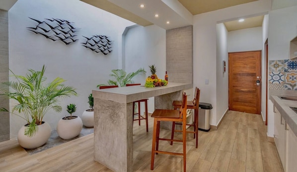 Cocina moderna con una isla central, sillas de madera, plantas en macetas y decoración mural.