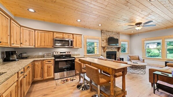 A kitchen with wooden cabinets, a central island with bar stools, a fireplace, and a stone wall.