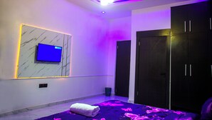 Un dormitorio moderno con televisor montado en una pared de mármol, cama con manta púrpura y armario oscuro.