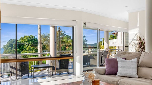 A spacious living room with large windows, a balcony, and a view of greenery and hills.