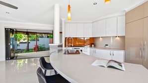 A modern kitchen with white cabinetry, a central island, and a view of a garden through glass doors.